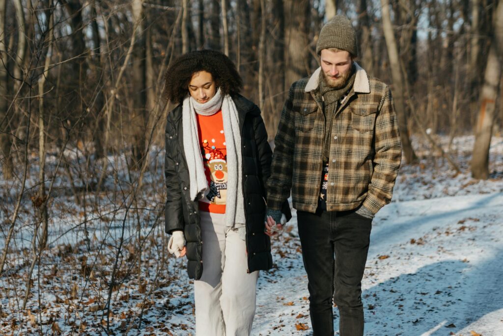 A couple holding hands while walking through a snow-covered forest during winter.